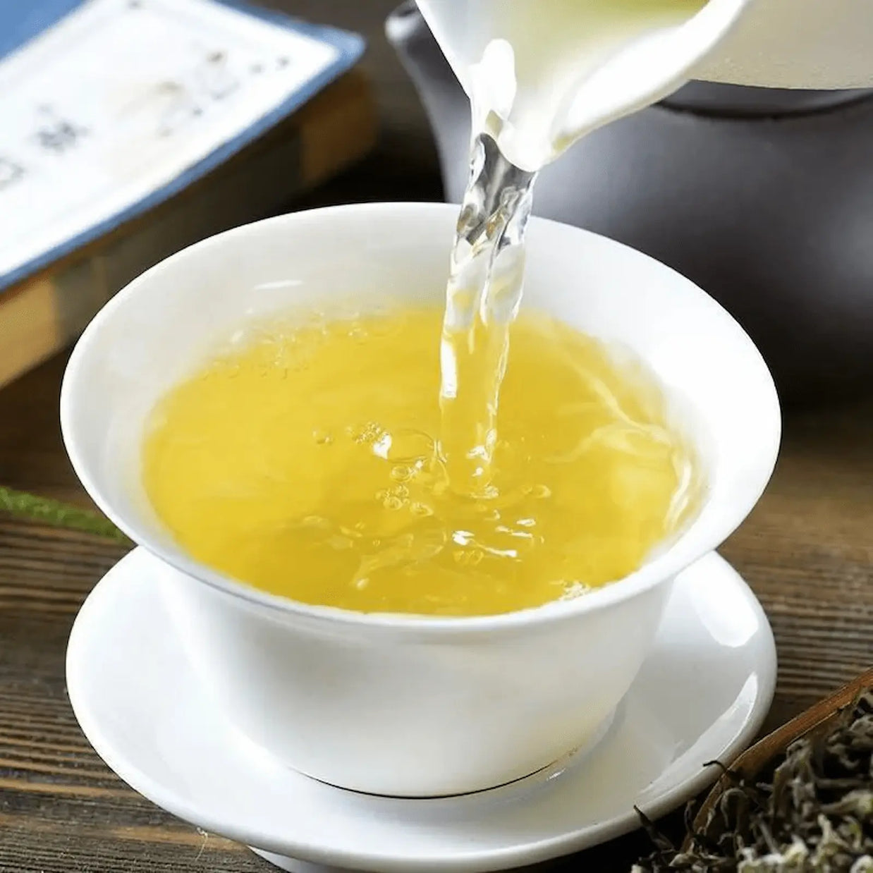 Pouring freshly brewed Bi Luo Chun green tea into a white porcelain cup, showcasing the bright yellow-green liquor. Authentic Chinese spring tea known for its delicate aroma and refreshing taste.
