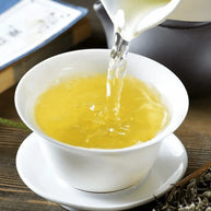 Pouring freshly brewed Bi Luo Chun green tea into a white porcelain cup, showcasing the bright yellow-green liquor. Authentic Chinese spring tea known for its delicate aroma and refreshing taste.
