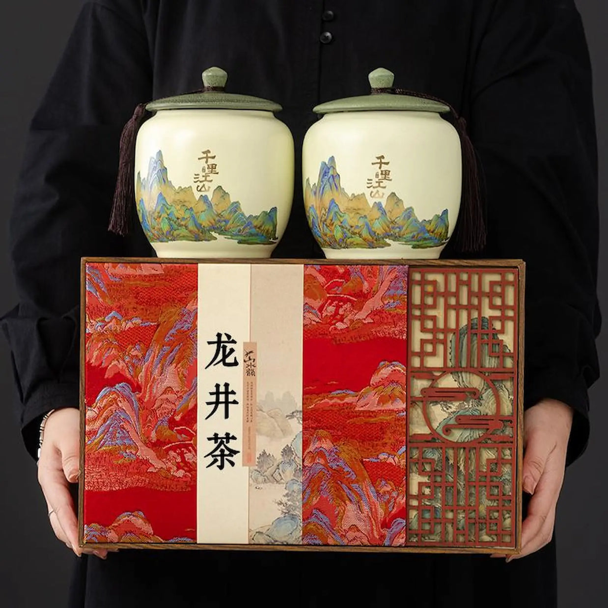 Deluxe West Lake Longjing green tea gift set with two ceramic jars and elegant red presentation box, featuring traditional Chinese landscape art. Perfect premium Xi Hu Dragon Well tea gift for festivals and special occasions.
