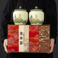 Deluxe West Lake Longjing green tea gift set with two ceramic jars and elegant red presentation box, featuring traditional Chinese landscape art. Perfect premium Xi Hu Dragon Well tea gift for festivals and special occasions.
