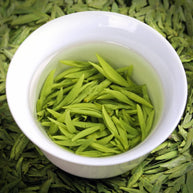Freshly steeped Ming Qian Longjing green tea leaves in a white porcelain cup, showcasing vibrant green buds and clear tea liquor. Premium pre-Qingming Dragon Well tea from Hangzhou, prized for its delicate aroma and mellow taste.
