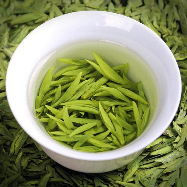 Freshly steeped Ming Qian Longjing green tea leaves in a white porcelain cup, showcasing vibrant green buds and clear tea liquor. Premium pre-Qingming Dragon Well tea from Hangzhou, prized for its delicate aroma and mellow taste.

