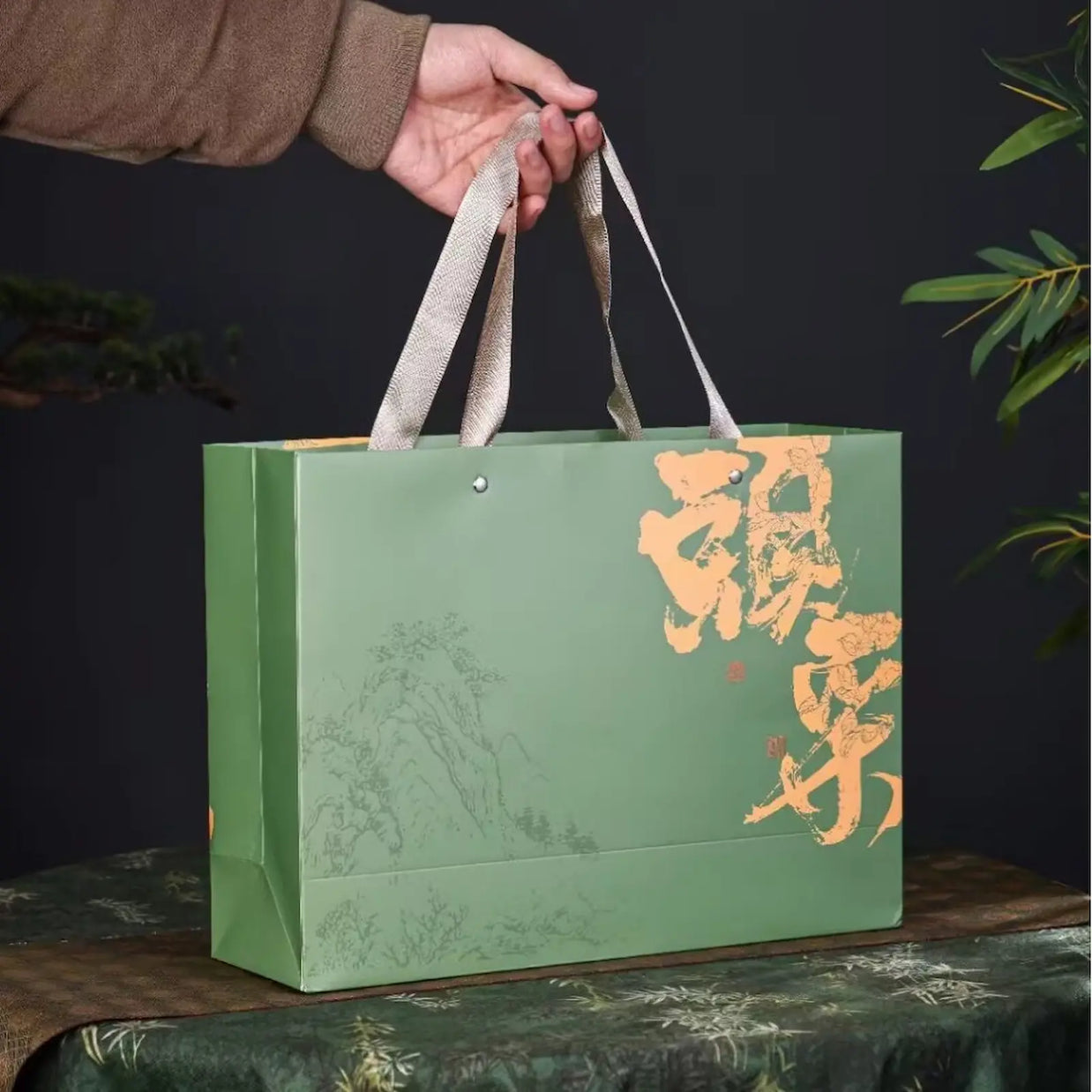 Green Ming Qian Longjing tea gift bag with traditional Chinese calligraphy and subtle landscape art, sturdy handles for easy carrying. Perfect for presenting premium pre-Qingming West Lake Dragon Well green tea on holidays and special occasions.
