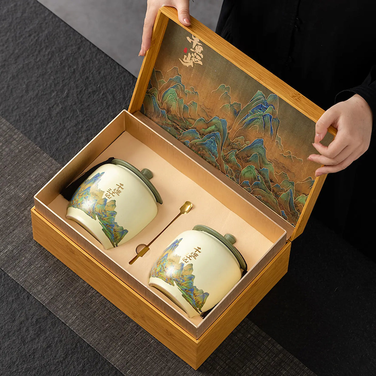 Luxury West Lake Longjing green tea gift set featuring two ceramic storage jars with traditional Chinese landscape design, presented in a premium bamboo box. Ideal for gifting authentic Xi Hu Dragon Well tea on special occasions.
