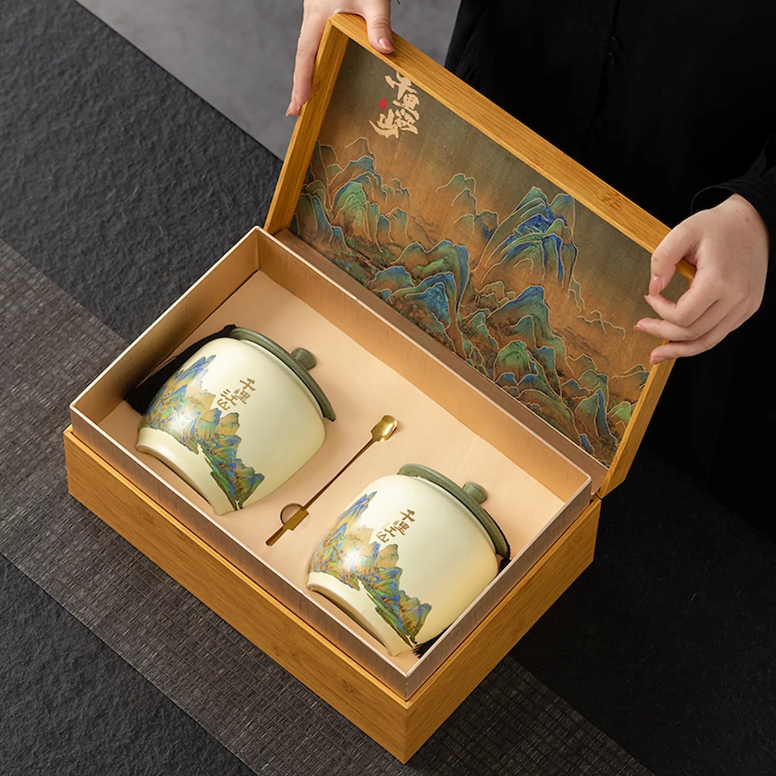 Luxury West Lake Longjing green tea gift set featuring two ceramic storage jars with traditional Chinese landscape design, presented in a premium bamboo box. Ideal for gifting authentic Xi Hu Dragon Well tea on special occasions.

