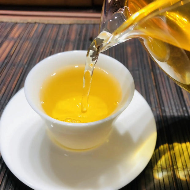 Pouring freshly brewed tea into a traditional white teacup, showcasing the vibrant golden liquor of premium green or oolong tea. Ideal for tea enthusiasts practicing Gongfu tea ceremony or enjoying a moment of relaxation.
