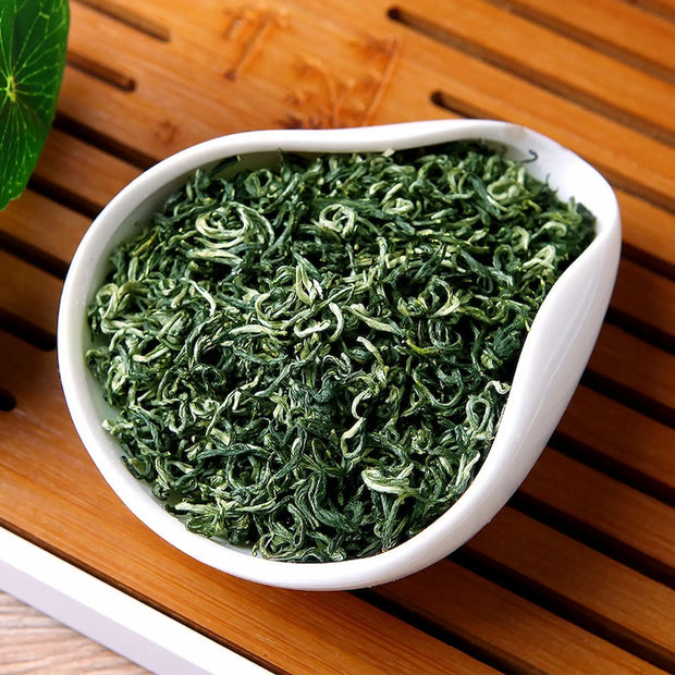 Premium Bi Luo Chun green tea leaves in a white porcelain dish, featuring delicate spiral shapes and fine white hairs. Authentic Chinese spring tea from Dongting Mountain, prized for its fresh aroma and mellow taste.
