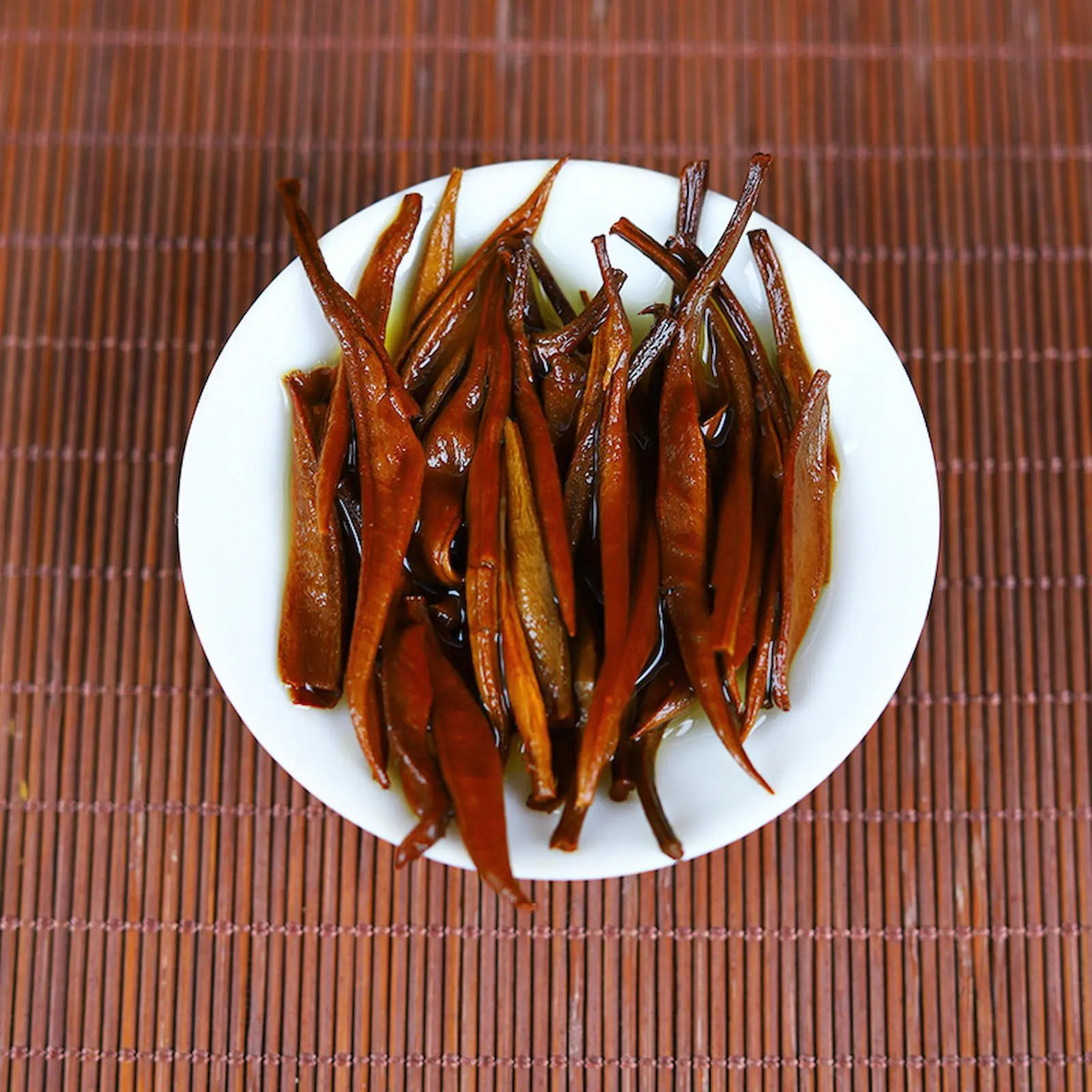 Steeped Yunnan Golden tea leaves in a white bowl, displaying rich amber color and tender texture after brewing. Perfect representation of high-quality Dian Hong black tea from Yunnan, ideal for tea tastings and Chinese tea ceremonies.
