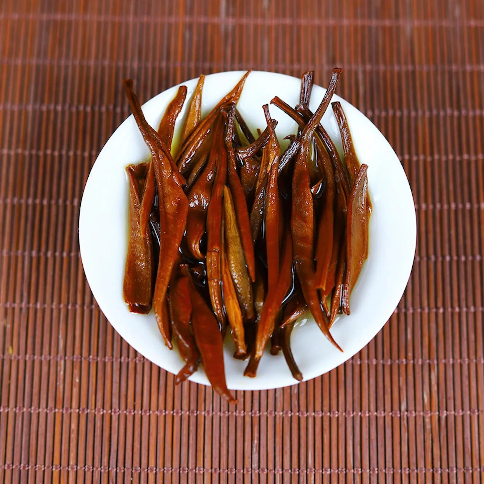 Steeped Yunnan Golden tea leaves in a white bowl, displaying rich amber color and tender texture after brewing. Perfect representation of high-quality Dian Hong black tea from Yunnan, ideal for tea tastings and Chinese tea ceremonies.
